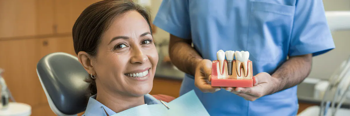 Patient smiling while a dentist holds an implant model